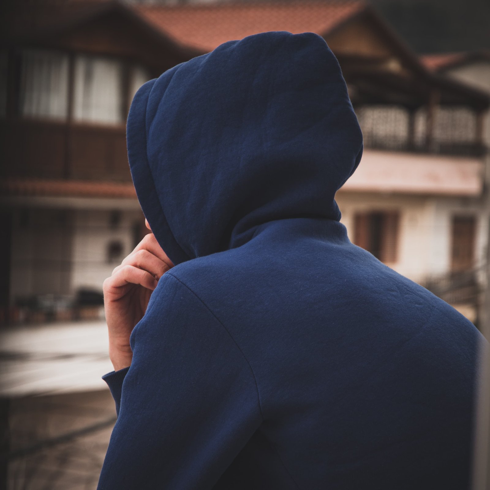 Person in a navy hooded sweatshirt seen from behind in a quiet residential setting