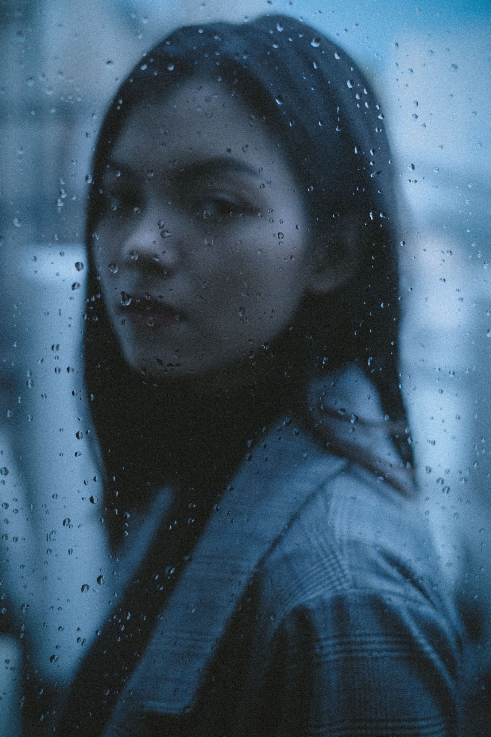 Person seen through a rain-covered window in a muted blue tone