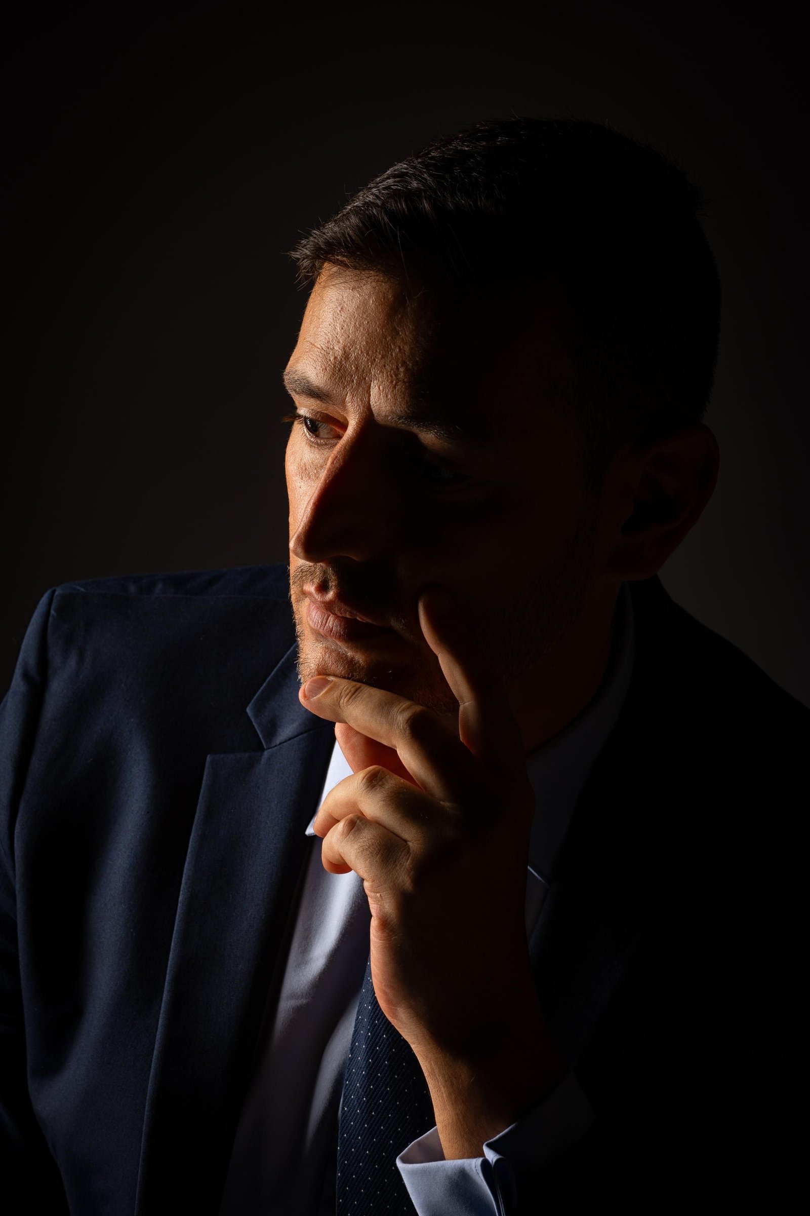 A person sitting in low light, resting their hand near their face.